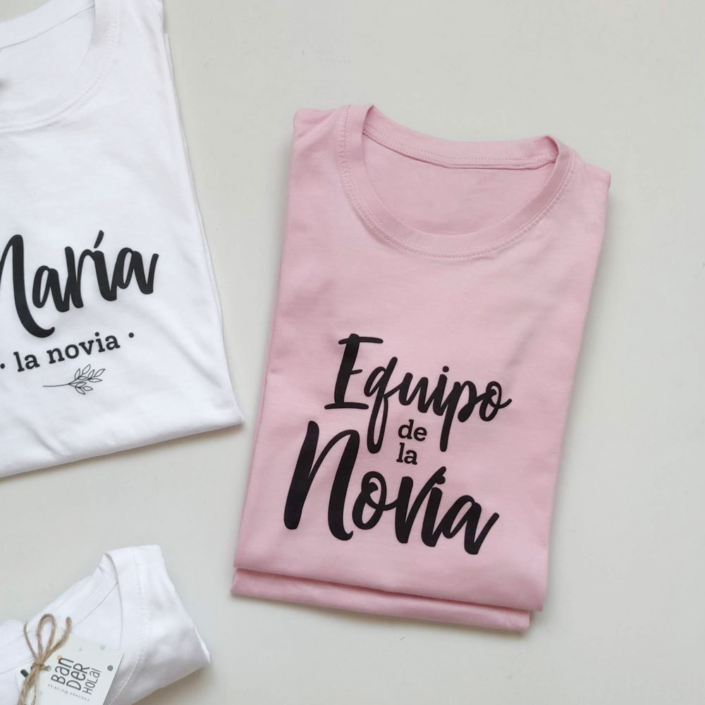 CAMISETA DESPEDIDA EQUIPO DE LA NOVIA ROSA CLARO DOBLADA JUNTO A CAMISETA BLANCA LA NOVIA